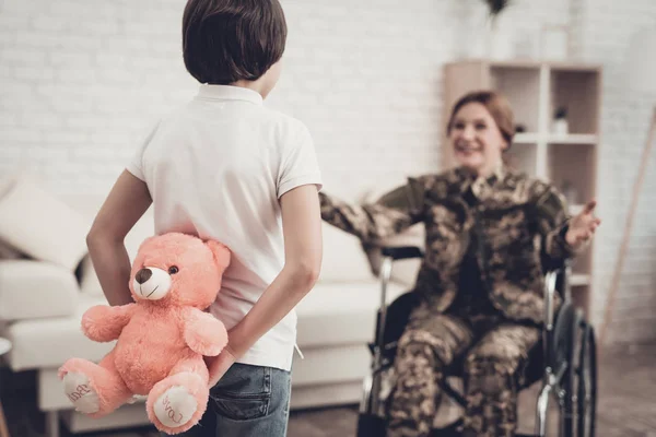 Woman Veteran In Wheelchair Homecoming Concept. Family Meeting. Leaving From War. Fluffy Toy. Camouflage Uniform. Son Hanging. Feelings Showing. Patriotic Comeback. Paralyzed Soldier.