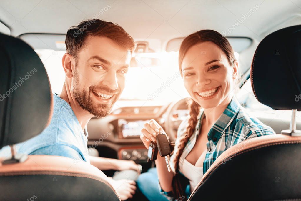 Smiling Couple Sitting In A Frontseat Of A New Car. Young Family. Automobile Salon. Cheerful Driver. Successful Buying. Good Mood. Great Trade. Sunny Windshield. Camera Posing.