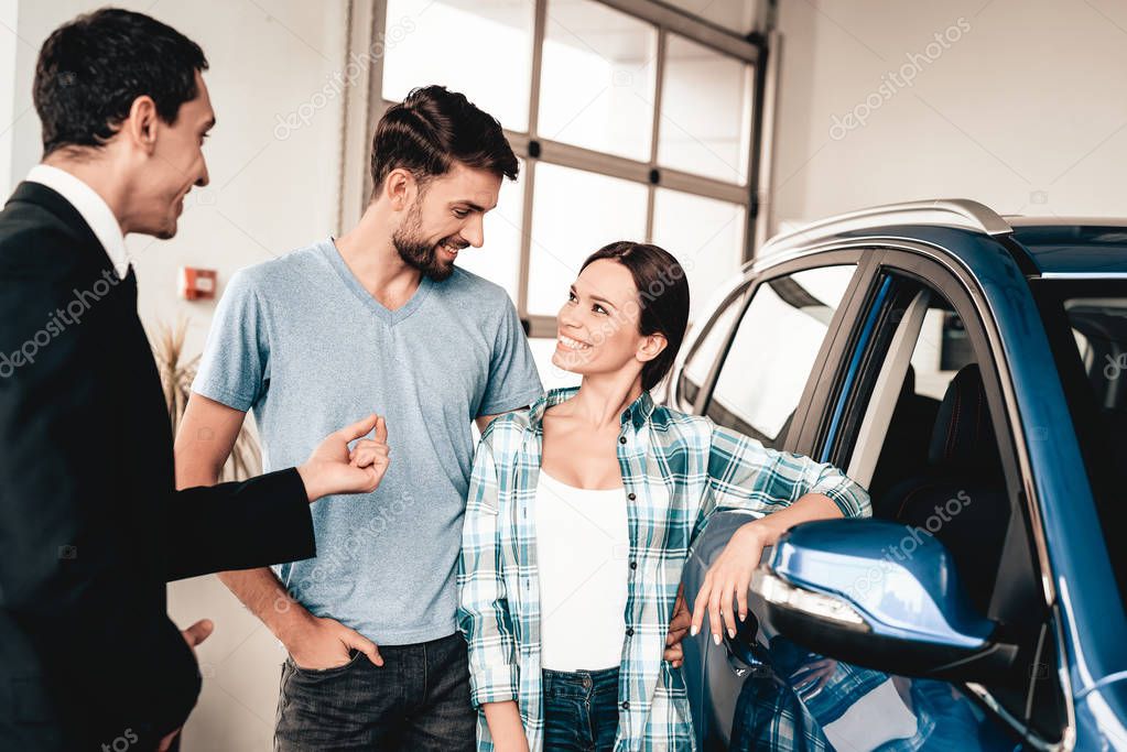 Happy Young Family Are Choosing A New Car In Showroom. Dialogue With Dealer. Cheerful Customer. Automobile Salon. Make A Decision. End Of A Deal. Good Offer. Buyer And Seller. Business Trade.