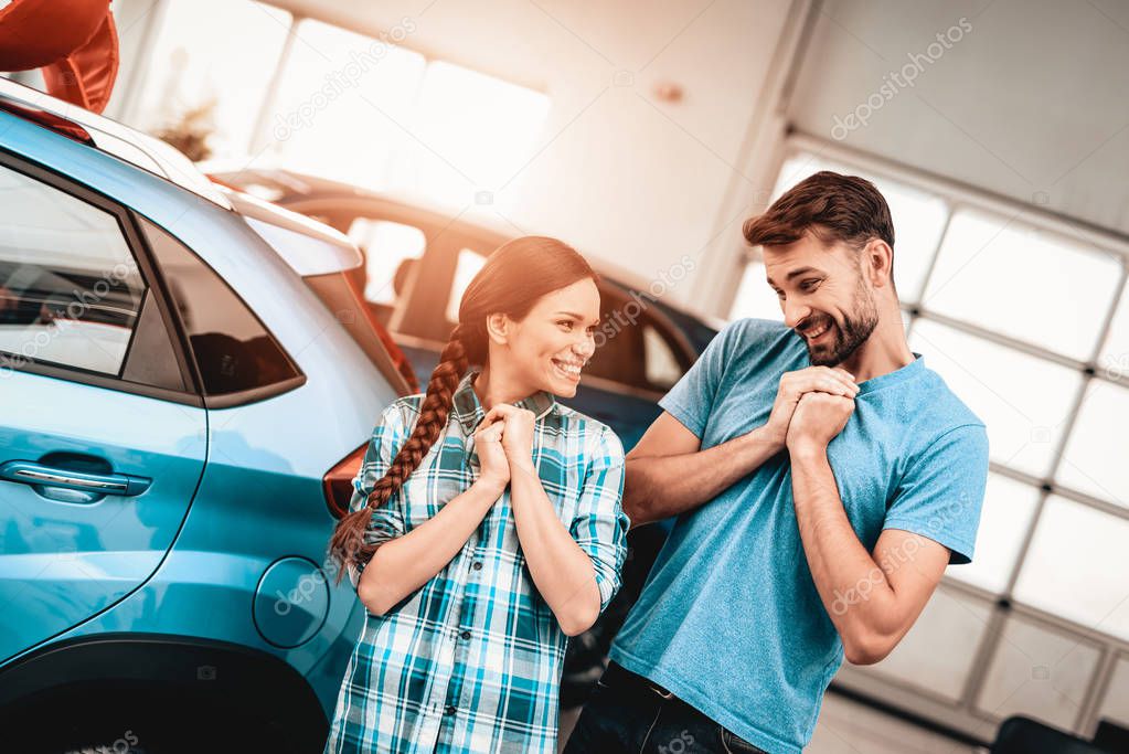 Young Family Are Choosing A New Car In Showroom. Staring At Each Other. Automobile Salon. Make A Decision. Gift Ribbon. End Of A Deal. Good Offer. Happy Together. Successful Buying.