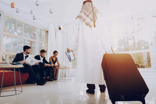 アラビア人ビジネスマンはオフィスでスーツケースを持っています お金の投資 紙のドキュメント ラップトップでの作業 飛行機のチケットディスダッシュとケフィエの着用 ジャーナルを読む 旅行に行く — ストック写真