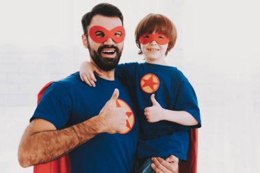Baba ve oğul. Kırmızı ve mavi süper kahraman takım elbise. Maskeleri ve yağmurluklar. Aydınlık bir salonda poz. Genç mutlu aile tatil kavramı. Birlikte dinleniyor. Dünyayı kurtarmak. Hazır olun. Çok iyi.