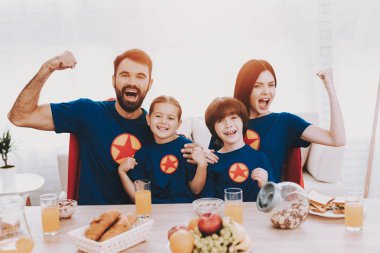 Süper kahraman takım elbiseli Genç mutlu aile. Akşam yemeği kavramı. T-shirt ve yağmurluklar. Parlak oda. Birlikte dinleniyor. Suyu ve tahıllar. Sağlıklı bir yaşam tarzı. Ebeveynler çocukları asılı olan. Etkin boş.