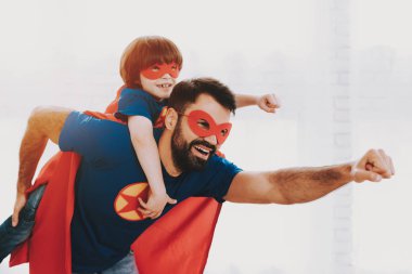 Baba ve oğul. Kırmızı ve mavi süper kahraman takım elbise. Maskeleri ve yağmurluklar. Aydınlık bir salonda poz. Genç mutlu aile tatil kavramı. Birlikte dinleniyor. Dünyayı kurtarmak. Hazır olun. Sağlam ve güçlü.