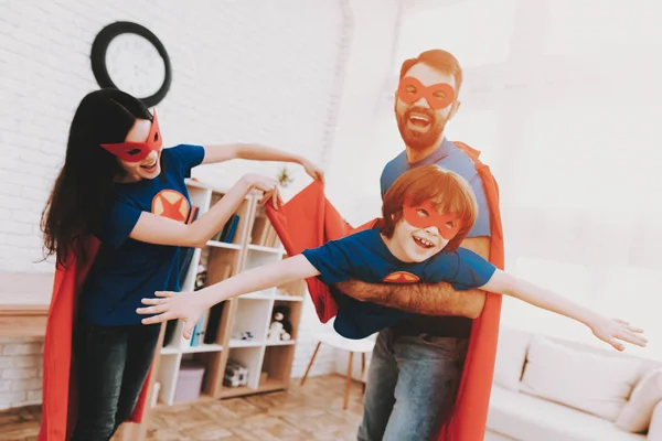 Mother, father and son in suits of superheroes. Incredibles in a bright room. Parents hold their son in their arms and play superheroes.