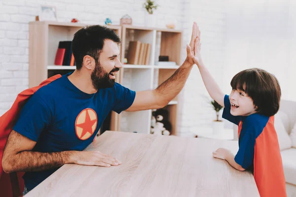 微笑的父亲和儿子 红色和蓝色的超级英雄西装 明亮的客房 年轻愉快的家庭假期概念 在一起休息 健康的生活方式 积极休闲 节日快乐 — 图库照片