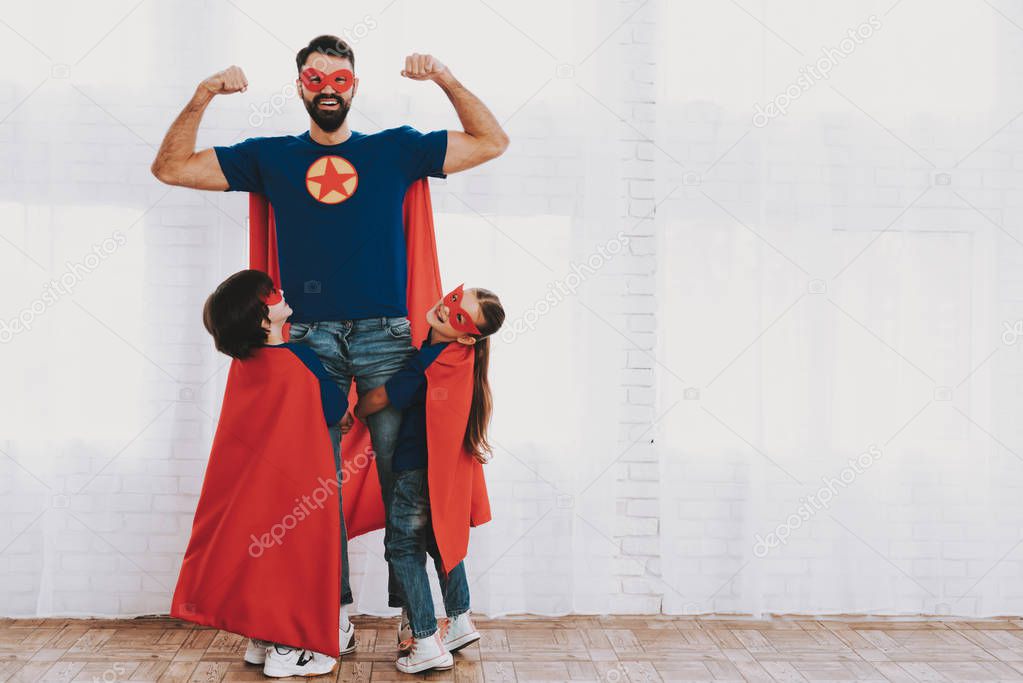 Young Family In Superhero Suits. Posing Concept. Masks And Raincoats. Bright Room. Resting Together. Save The World. Get Ready. Hand In Hand. Kids With A Parents. Active Lifestyle.