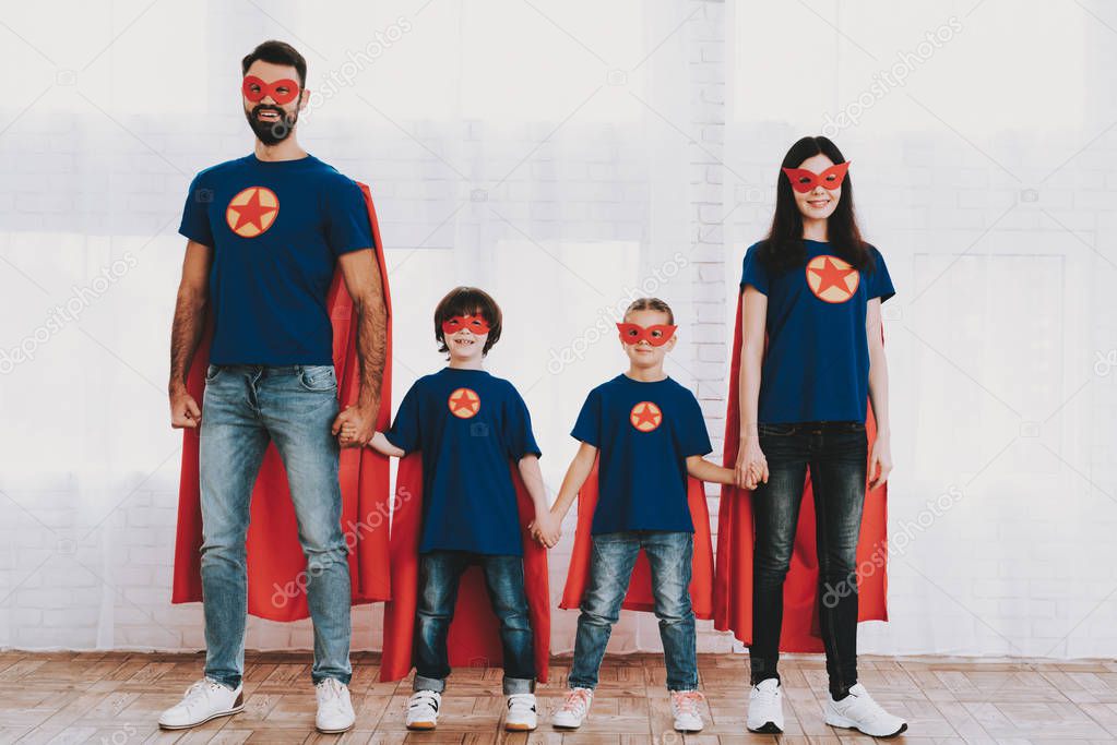 Young Family In Superhero Suits. Posing Concept. Masks And Raincoats. Bright Room. Resting Together. Save The World. Get Ready. Hand In Hand. Kids With A Parents. Active Lifestyle.