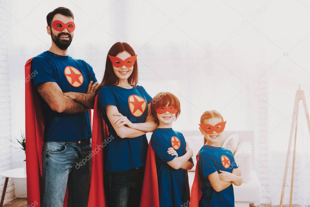 Young Family In Superhero Suits. Posing Concept. Masks And A Raincoats. Bright Room. Resting Together. Save The World. Get Ready. Arms Akimbo. Kids With A Parents. Active Lifestyle.