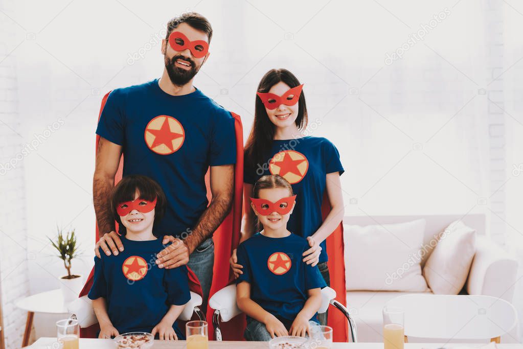 Young Happy Family In Superhero Suits. Dinner Concept. Masks And Raincoats. Bright Room. Resting Together. Juice And Cereals. Get Ready. Healthy Lifestyle. Parents Are Hanging Kids.