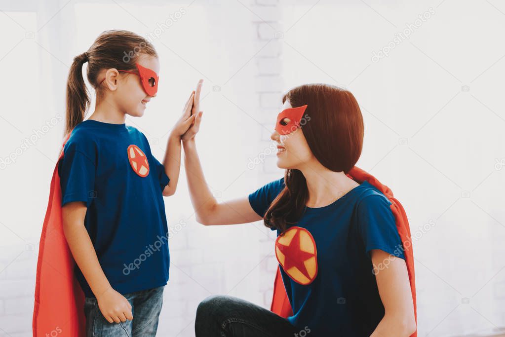 Mother And Daughter. Red And Blue Superhero Suits. Masks And Raincoats. Posing In A Bright Room. Young Happy Family Holiday Concept. Resting Together. High Five. Strong And Powerful.