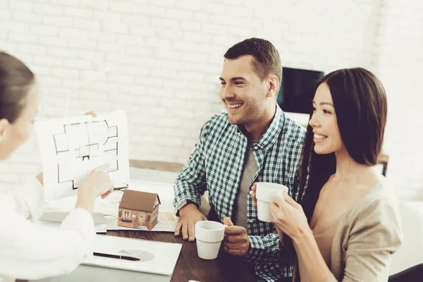 Young Man and Woman with Smiling Realtor in Office. Blueprint on Wooden Desk. Real Estate Concepts. Young Couple. Buying New Home. Family in Office. Rental Agent Concept. Happy Family.