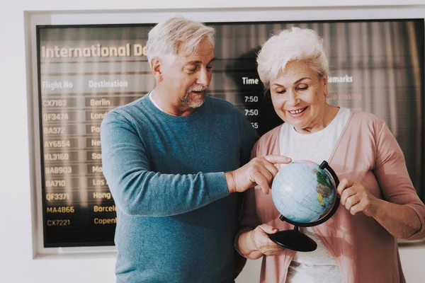 Old Couple with Globe in Airport in Waiting Room. Senior Person in Airport. Tourism Concept. Old Couple in Voyage. Airport Terminal. Vacation for Pensioner. People with Baggage. Travelers on Vacation.