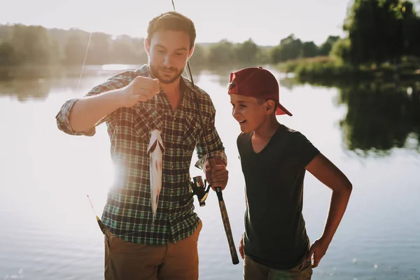 年轻的父亲与儿子在盖帽捕鱼在河上在夏天 放松的户外 带着胡子的年轻人 湖边的男人 手里拿着钓鱼竿 夏天的运动 周末在河上 年轻的渔夫 — 图库照片