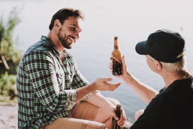 Yaz aylarında Nehri yakınında gülümseyen adam içki bira. Tişörtlü adam. Sakallı adam. Nehri üzerinde hafta sonu. Genç adam açık rahatlatıcı. Adam adam göl kenarında oturuyor. İçki içerken. Bira şişe.