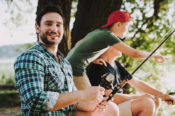 Young Man with Son and Father Fishing on River in Summer. Relaxing Outdoor. Old Man and Boy. Men near Lake. Fishing Rod in Hands. Sports in Summer. Weekend on River. Aged Fisherman.