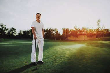 Golf sahasında oynayan beyaz giysili genç adam. Golf Club civarındaki rahatlatıcı. Spor yaz. Yaz aylarında açık eğlenceli. Mutlu genç adam sağlıklı yaşam konsepti. Beyaz gömlek dostum. Yeşil çimen.