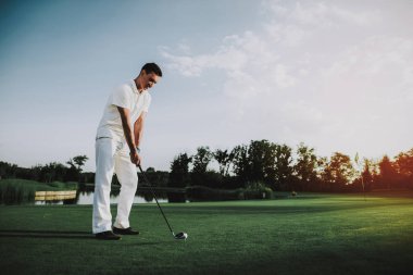 Golf sahasında oynayan beyaz giysili genç adam. Golf Club civarındaki rahatlatıcı. Spor yaz. Yaz aylarında açık eğlenceli. Mutlu genç adam sağlıklı yaşam konsepti. Beyaz gömlek dostum. Yeşil çimen.