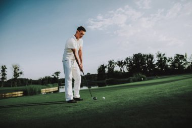 Golf sahasında oynayan beyaz giysili genç adam. Golf Club civarındaki rahatlatıcı. Spor yaz. Yaz aylarında açık eğlenceli. Mutlu genç adam sağlıklı yaşam konsepti. Beyaz gömlek dostum. Yeşil çimen.