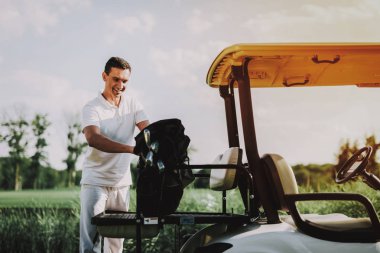 Golf sahasında sepeti kullanarak Beyaz tişörtlü genç adam. Mutlu genç adam sürücü araba ile. Sağlıklı yaşam konsepti. Golf Kulübü. Spor yaz. Araç alan üzerinde. Aile tatili. Yaz aylarında açık eğlence.