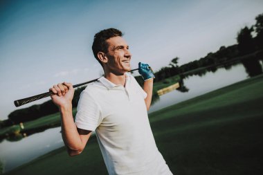 Golf sahasında oynayan beyaz giysili genç adam. Golf Club civarındaki rahatlatıcı. Spor yaz. Yaz aylarında açık eğlenceli. Mutlu genç adam sağlıklı yaşam konsepti. Beyaz gömlek dostum. Yeşil çimen.