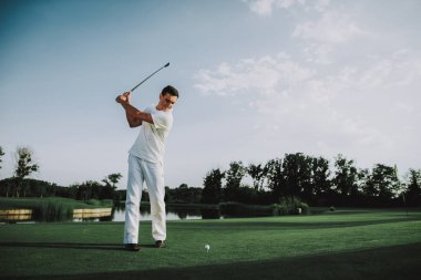 Golf sahasında oynayan beyaz giysili genç adam. Golf Club civarındaki rahatlatıcı. Spor yaz. Yaz aylarında açık eğlenceli. Mutlu genç adam sağlıklı yaşam konsepti. Beyaz gömlek dostum. Yeşil çimen.