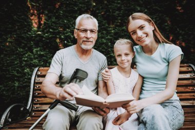 Yaşlı adam ve aile sit bankta ile. Aile ile iyi bir yaşlı adam terapi yaş gülümse. Kitap ailesi ile rehabilitasyon ve reed. Hemşire ile profesyonel yardım. Hastalık ve rehabilitasyon yaşlı adam.