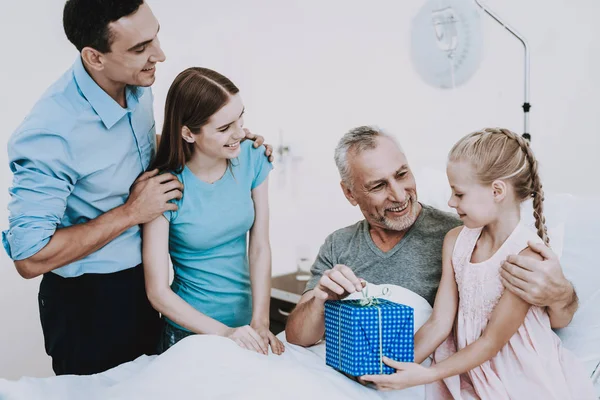 Clinic Room with Family. Good Gift for Aged. Surprise for Old Man and Child. Medical and People in our Life. Family Help Old Man with Disease. Family Care about Old Man. Therapy in White Room For Man.