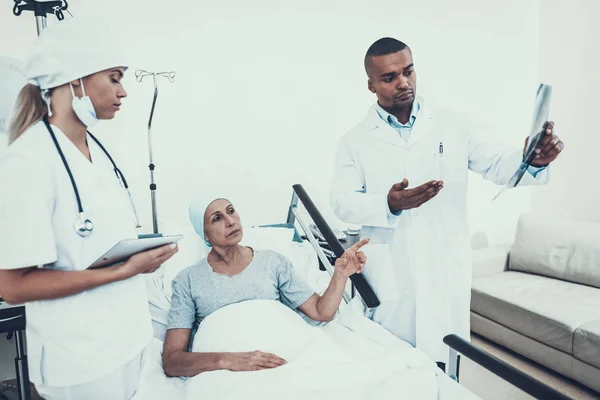 Doctor and Nurse in Ward. Woman Undergoes Rehabilitation. After Treatment for Cancer. Nurse's Notes. Woman on Bunk. Doctor looks at the X-ray. Doctor in Clinic. Cancer Patient. Scarf on Woman's Head.