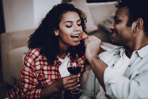 Boyfriend Is Feeding Girlfriend With Strawberry. Weekend Concept. Chilling On Sofa. Holiday Resting. Smiling Together. Having Fun. Romantic Date. Afro American Couple Drinking Wine.