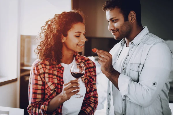 Boyfriend Is Feeding Girlfriend With Strawberry. Weekend Concept. Chilling At Kitchen. Holiday Resting. Smiling Together. Having Fun. Romantic Date. Afro American Couple Drinking Wine.