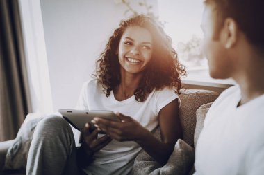 Afro Amerikan çift kanepede becerikli alet ile. Sabah eğlence. Mola verebilir. Ekrana bak. Kanepenin üzerinde tüyler ürpertici. Ev giysileri. Tatil dinlenme. Birlikte gülümseyen. Dizüstü ve Tablet.