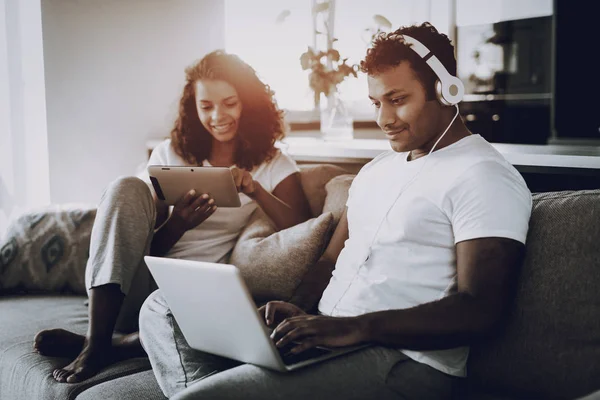 美国黑人夫妇在沙发上的小玩意 上午休闲 休息一下 看屏幕上 在沙发上冷 家庭服 假期休息 一起微笑 笔记本电脑和平板电脑 — 图库照片