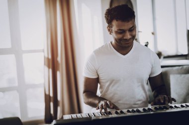 Afro Amerikalı genç adam Synthesizer evde oynuyor. Mutlu şarkı sözü yazarı. Sabah eğlence. Dijital formatta ses kaydı. Çalışma müzisyen. Müzikal hobi. Eller klavye. Neşeli Professional.