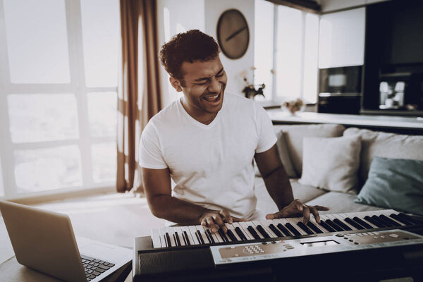 Афро-американский юноша играет в синтезатор дома и поет. Счастливого автора песен. Утренний отдых. Цифровая звуковая запись. Работающий музыкант. Музыкальное хобби. Руки на клавиатуре
.