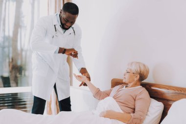 Önlemler nabız ve basınç. Doktor inceliyor. Yaşlı hasta. Bakım evi. Yatakta yatıyordu. Konuş. Gülümseyen doktor. Sick.Interviews hissediyorum. Doktor dolgular Form. Kadınların durumu hakkında söyle. Kağıtları erkeklerle.