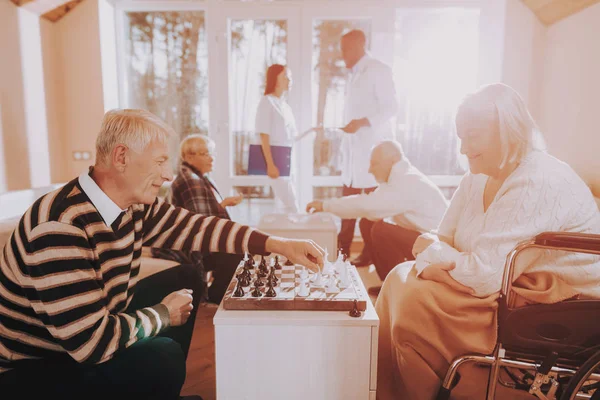 Elderly. Male. Patient. Patient on a Wheelchair. Senior Man and Woman. Play Chess. Nursing Home. Black. Doctor. Asian. Nurse. Stand Nearby. Rehabilitation. Sitting Woman. Young and Old People.