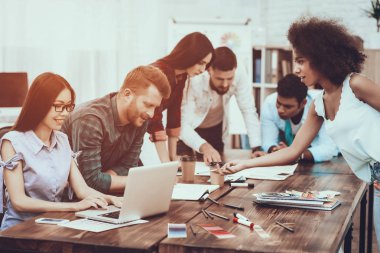 Bir grup genç insan. Dizüstü bilgisayar. Kalem. Not defteri. Proje. Ekip çalışması. Çalışma masaları. Büyük parlak Office. İşbirliği. Farklı uluslardan. Beyin fırtınası harcamak. İş. Tablo. Renk örnekleri. Tasarım.