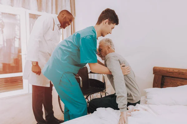 Get Out of Bed. Nurse Helps. Elderly Man. Sit in Wheelchair. It\'s Hard to Do. Man Feels Weak. Doctor in Clinic. Doctor Helps get up. Patient. Patient on a Wheelchair. Nursing Home. Rehabilitation.