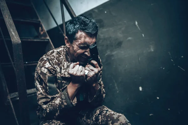 Man Is Sitting In War Shelter With Shotgun. Camouflage Uniform. Military Actions. War Hideaway Concept. Occupation Problem. Depressed Soldier. Disappointed Hero. Posttraumatic Syndrome.