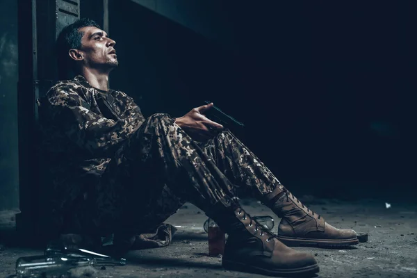 Man Is Sitting In War Shelter With Shotgun. Camouflage Uniform. Military Actions. War Hideaway Concept. Bottle With Alcohol. Occupation Problem. Depressed Soldier. Disappointed Hero.