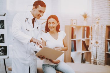 Beyaz önlük. Doktor. Dizüstü bilgisayarda gösterilen. Danışma. Hastane. Doğum sırasında. Göbek. Hamile kadın. Gülümseyerek. Kliniği. Jinekolog. Kliniği. Annelik. Dizüstü bilgisayar. İyi eğlenceler. Tıbbi yardım.