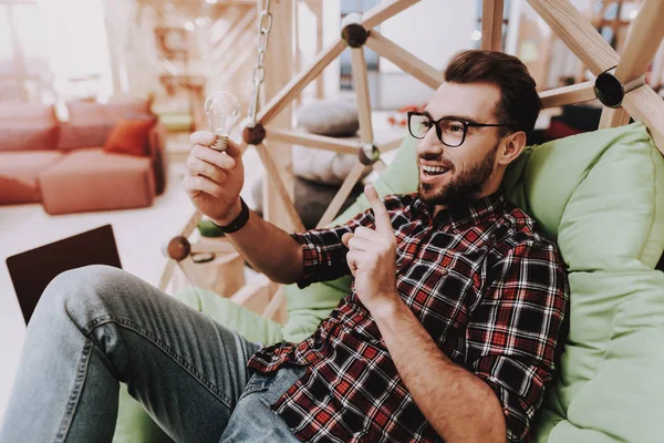 Yaratıcı işçi. Dizüstü bilgisayar. Ampul. Fikirler oluşturur. Sandalyeye asılı. Otur. Beyin fırtınası. Genç bir adam. İş adamı. Ofiste çalışıyor. İş adamları. Çalışma alanı. İlham. Gevşeme. Rahat Office.