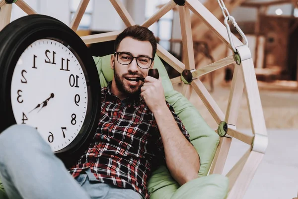 Big Watch. Hanging Chair. Clock. Eyeglasses. Young Male. Businessman. Working in Office. Creates Ideas. Eyeglasses. Workplace. Project. Sit. Brainstorm. Work. Office. Creative Worker. Inspiration.