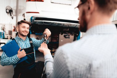 Otomatik mekanik tuşları garajda araba sahibine verir. Güven haklı. Profesyonel üniforma. Kendine güvenen mühendis bakışları. Onarım genç uzman. Servis istasyonu kavramı. Makine tamir.