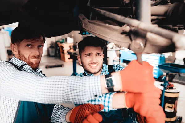 Young Mechanic Repairs Automotive Hub In Garage. Professional Uniform. Service Station Concept. Confident Engineer Stare. Detail Repairing. Under The Vehicle. Automobile Diagnostic. Join Forces.