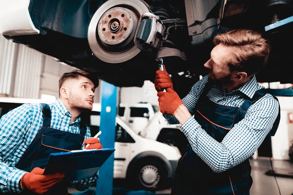 若いメカニックは修理のガレージで自動車のハブです プロのユニフォーム サービス ステーション 自信を持ってエンジニアを見詰める 詳細を修復します 車の下で 自動車診断 — ストック写真