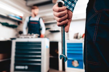 Yakın çekim. Adam anahtarı meslektaşım önünde tutar. Otomatik mekanik işçi kavramı. Servis İstasyonu. Profesyonel üniforma. Kendine güvenen mühendislik uzman ekip. Kızıl saçlı tamirci arka plan.