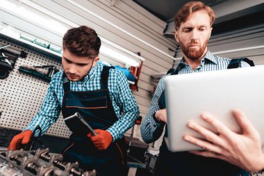 İki otomatik mekanik birlikte garajda çalışır. Kullanarak anahtarı. Dizüstü ekran bakıyor. Bilgi paylaşımı. Profesyonel üniforma. Kendine güvenen mühendislik uzman ekip. Servis istasyonu kavramı.