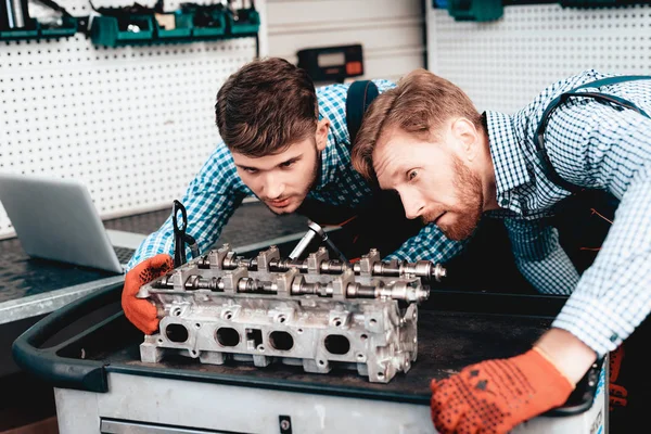 Two Auto Mechanics Are Checking Detail In Garage. Professional Uniform. Confident Engineering Specialist Stare. Protective Gloves. Working In The Garage. Young Repairman Posing Concept.